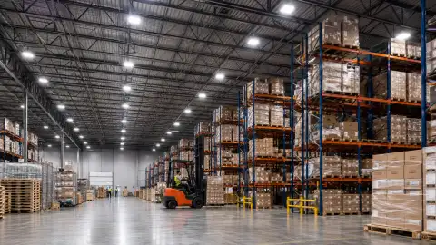 LED high-bay lighting retrofit inside a large warehouse with pallet racking and illuminated aisles